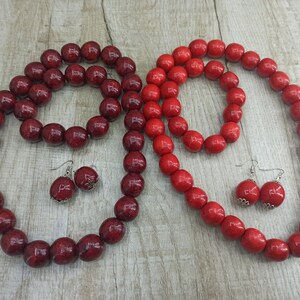 May include: A set of red wooden bead jewelry, including a necklace, bracelet, and earrings. The beads are large and round, and the jewelry is made with silver-toned metal.