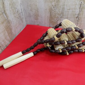 May include: A wooden massage tool with a series of spiked rollers connected by brown wooden beads. The tool has two wooden handles.
