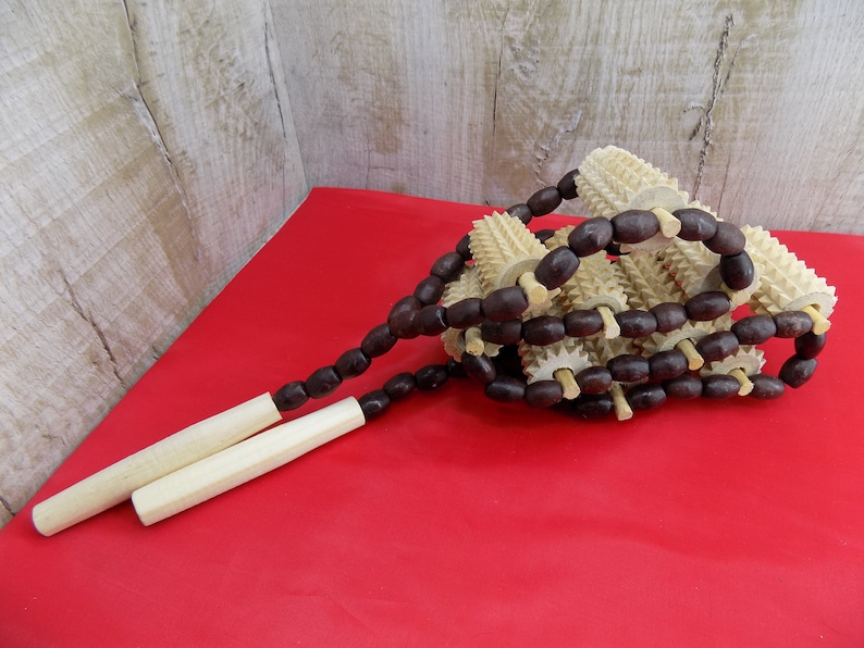May include: A wooden massage tool with a series of spiked rollers connected by brown wooden beads. The tool has two wooden handles.