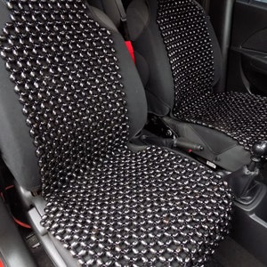 Puede incluir: Fundas de asiento de coche con cuentas negras. Las fundas están hechas de pequeñas cuentas redondas y oscuras unidas para formar un patrón similar a una malla. Las cuentas están dispuestas para cubrir el asiento y el respaldo de los asientos del coche. Los asientos del coche son negros.