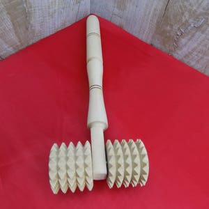 May include: A wooden rolling pin with two textured wheels. The wheels have a starburst pattern and are made of light brown wood. The rolling pin is on a red surface.