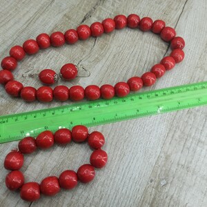 May include: A set of red wooden bead jewelry, including a necklace and a bracelet. The necklace is longer than the bracelet and both are made of round beads.
