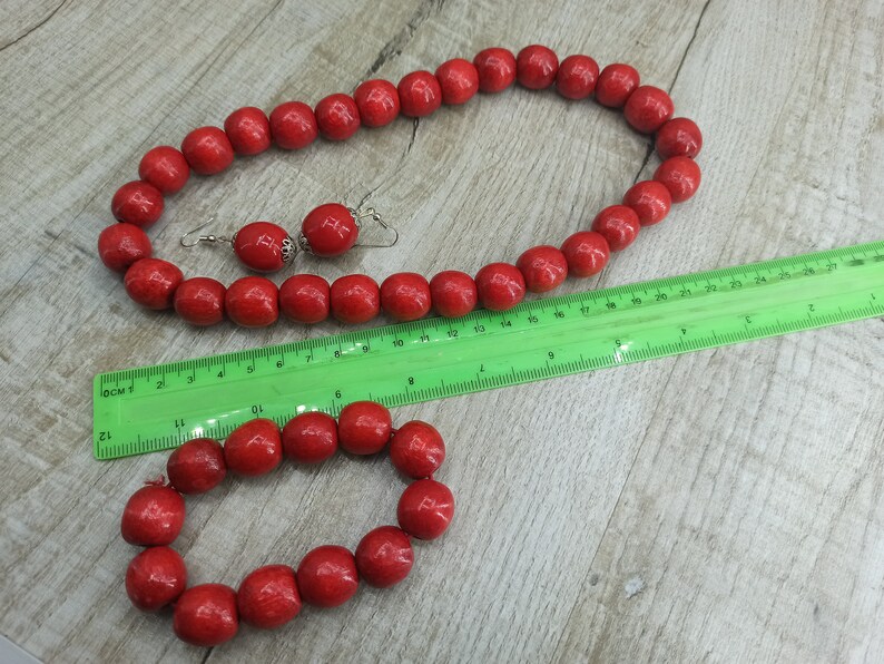 May include: A set of red wooden bead jewelry, including a necklace and a bracelet. The necklace is longer than the bracelet and both are made of round beads.