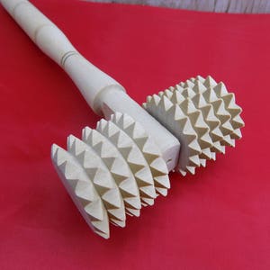 May include: A wooden rolling pin with a handle and two sets of spiked wheels. The wheels are made of wood and have a light brown color.