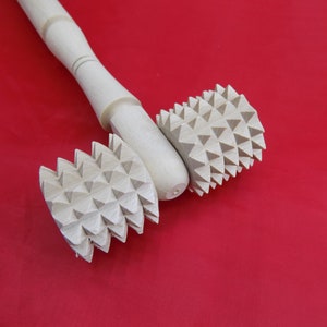 May include: A wooden rolling pin with two spiked wheels. The wheels are made of wood and have a triangular pattern.
