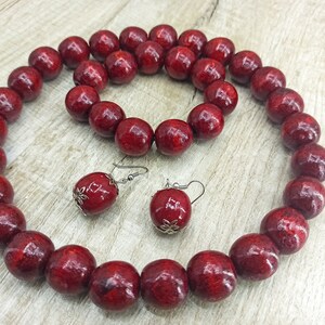May include: A set of red wooden bead jewelry, including a necklace and earrings. The necklace is made of large, round beads and the earrings are simple and dangle.