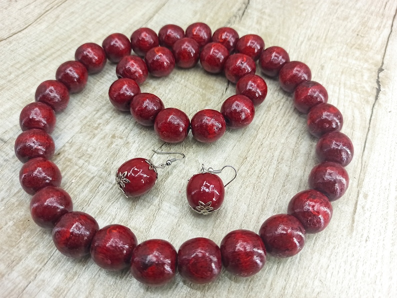 May include: A set of red wooden bead jewelry, including a necklace and earrings. The necklace is made of large, round beads and the earrings are simple and dangle.