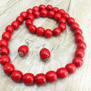 May include: A red wooden bead necklace, bracelet, and earrings set. The necklace and bracelet are made of large, round beads. The earrings are simple and dangle.