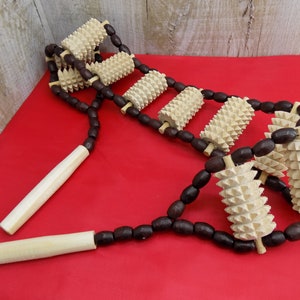 May include: A wooden back massager with brown wooden beads and multiple spiked rollers. The massager is on a red surface.