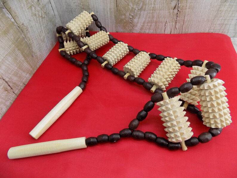 May include: A wooden back massager with brown wooden beads and multiple spiked rollers. The massager is on a red surface.