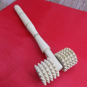 May include: A wooden rolling pin with two spiked wheels. The wheels have a starburst pattern. The rolling pin is on a red surface.