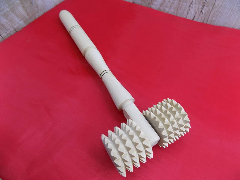 May include: A wooden rolling pin with two spiked wheels. The wheels have a starburst pattern. The rolling pin is on a red surface.