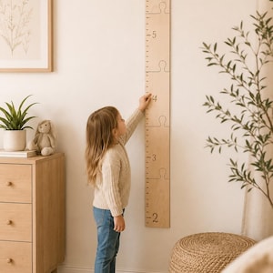May include: A light-colored wooden growth chart wall decal featuring puzzle-piece segments and black numerical markings from 2 to 6 feet. The top section is engraved with the text The Smith Family in a cursive script font.