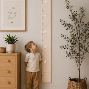 May include: A light-colored wooden growth chart mounted on a wall, featuring puzzle-piece segments and white numbers from 1 to 6. The vertical ruler displays precise measurement markings along its side, constructed from smooth, natural-toned wood.
