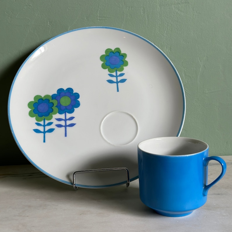 Puede incluir: Un plato de cer&aacute;mica blanco con un dise&ntilde;o floral azul y verde y una taza de t&eacute; de cer&aacute;mica azul a juego. El plato tiene un peque&ntilde;o platillo en el centro.