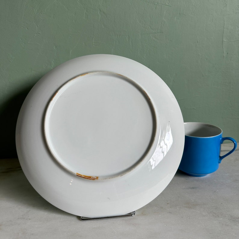 Puede incluir: Plato de cer&aacute;mica blanco con borde dorado. El plato se muestra desde la parte inferior, revelando una superficie lisa y blanca.