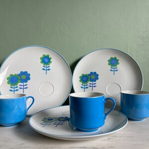 Puede incluir: Un juego de cuatro tazas de t&eacute; y platillos de cer&aacute;mica con estampado floral azul y blanco. Las tazas y los platillos tienen un dise&ntilde;o sencillo con flores azules y tallos verdes sobre un fondo blanco.