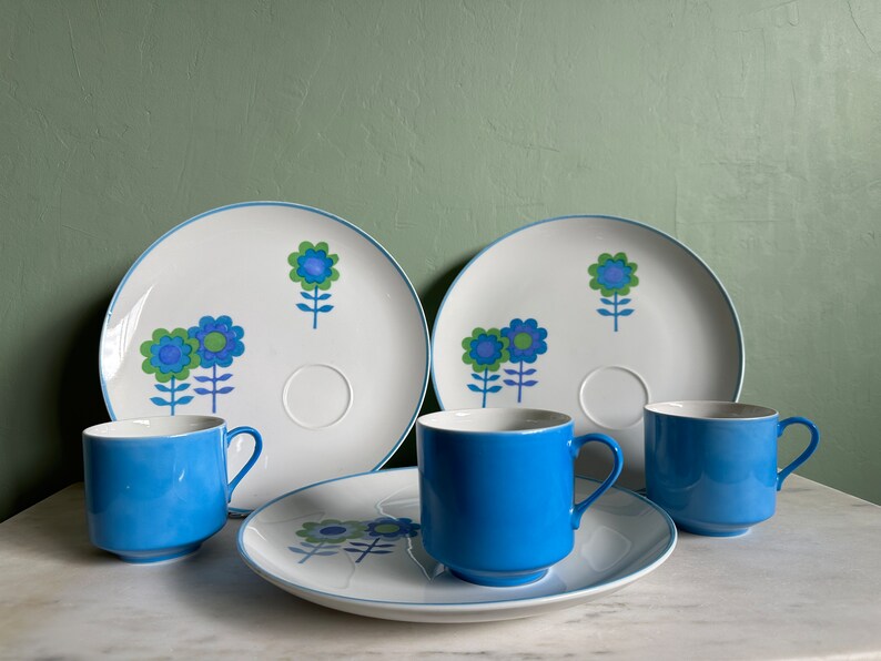 Puede incluir: Un juego de cuatro tazas de t&eacute; y platillos de cer&aacute;mica con estampado floral azul y blanco. Las tazas y los platillos tienen un dise&ntilde;o sencillo con flores azules y tallos verdes sobre un fondo blanco.