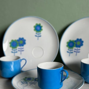 Puede incluir: Un juego de cuatro tazas de t&eacute; y platillos con estampado floral azul y blanco. Las tazas son de color azul s&oacute;lido y los platillos tienen un fondo blanco con dise&ntilde;os florales azules y verdes.