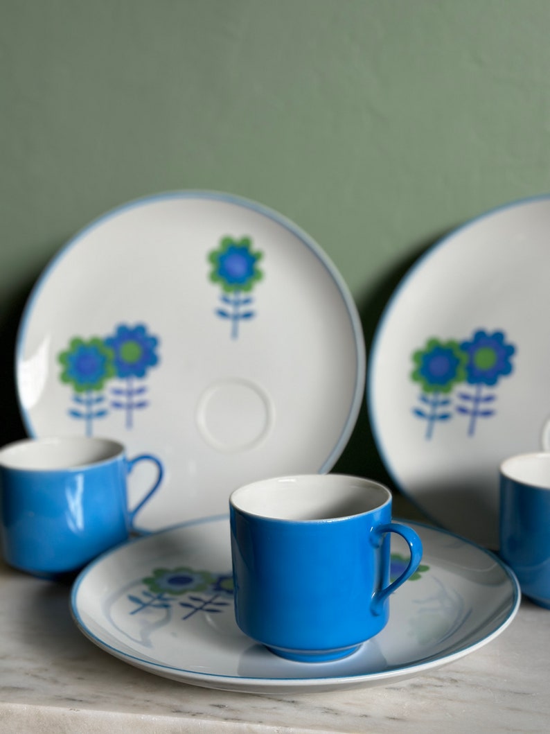 Puede incluir: Un juego de cuatro tazas de t&eacute; y platillos con estampado floral azul y blanco. Las tazas son de color azul s&oacute;lido y los platillos tienen un fondo blanco con dise&ntilde;os florales azules y verdes.