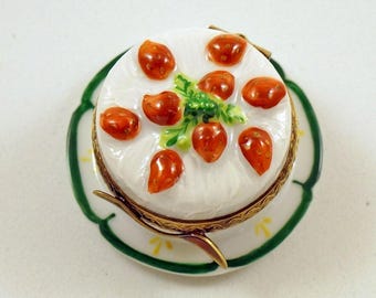 Puede incluir: Un pastel de porcelana blanca con fresas rojas y hojas verdes en la parte superior, sentado en un plato de porcelana verde y blanco.