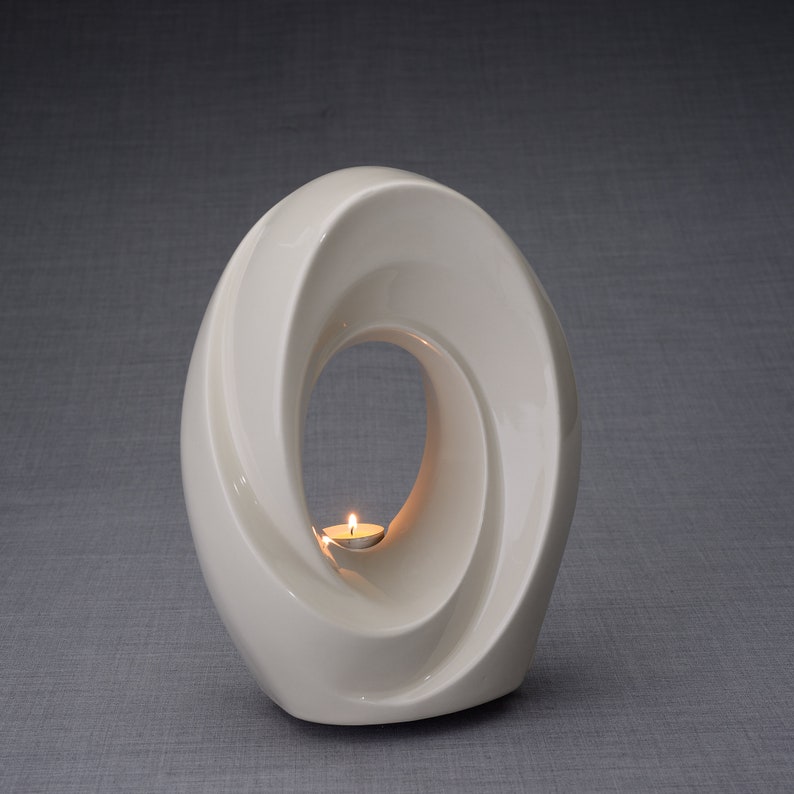 The Passage is a unique art urn for ashes. It represents a spiral, a vortex with a hole in the middle. The ashes go inside the walls and there is a candle that when lit reflects on the inner side of the art urn. This urn comes in a transparent color.