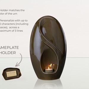 May include: A dark brown, egg-shaped urn with a glossy finish. A small candle burns inside a recessed area. A nameplate holder is included. The text on the nameplate holder reads "PULVIS".