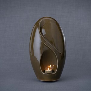 Adult size urn for ashes Eternity. The urn represents a straight ellipse with a hint of the infinity symbol all along its length. There is a place for a candle in the bottom half of the urn. This ceramic art urn comes in a various colors. By Pulvis