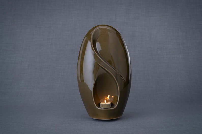 Adult size urn for ashes Eternity. The urn represents a straight ellipse with a hint of the infinity symbol all along its length. There is a place for a candle in the bottom half of the urn. This ceramic art urn comes in a various colors. By Pulvis
