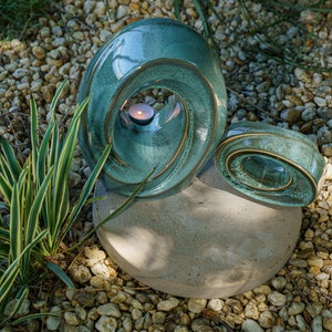 This unique keepsake urn represents a horizontal ellipse with a hole in the middle. Shaped as a spiral, a vortex, this handmade memorial urn holds the ashes in its walls. Set of urns The Passage large urn and keepsake.