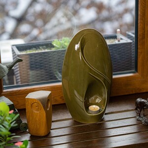 Adult size urn for ashes Eternity. The urn represents a straight ellipse with a hint of the infinity symbol all along its length. There is a place for a candle in the bottom half of the urn. This ceramic art urn comes in a various colors. By Pulvis