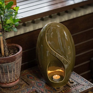 Adult size urn for ashes Eternity. The urn represents a straight ellipse with a hint of the infinity symbol all along its length. There is a place for a candle in the bottom half of the urn. This ceramic art urn comes in a various colors. By Pulvis