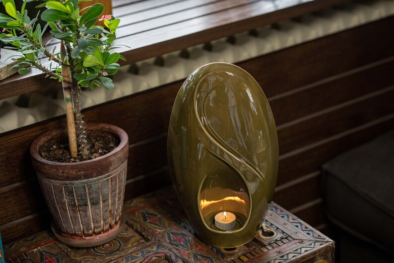 Adult size urn for ashes Eternity. The urn represents a straight ellipse with a hint of the infinity symbol all along its length. There is a place for a candle in the bottom half of the urn. This ceramic art urn comes in a various colors. By Pulvis