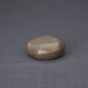 May include: A smooth, light brown stone with a slightly oval shape. The stone has a subtle sheen and a textured surface.