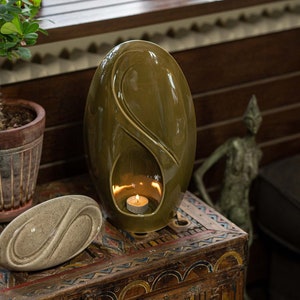 Adult size urn for ashes Eternity. The urn represents a straight ellipse with a hint of the infinity symbol all along its length. There is a place for a candle in the bottom half of the urn. This ceramic art urn comes in a various colors. By Pulvis