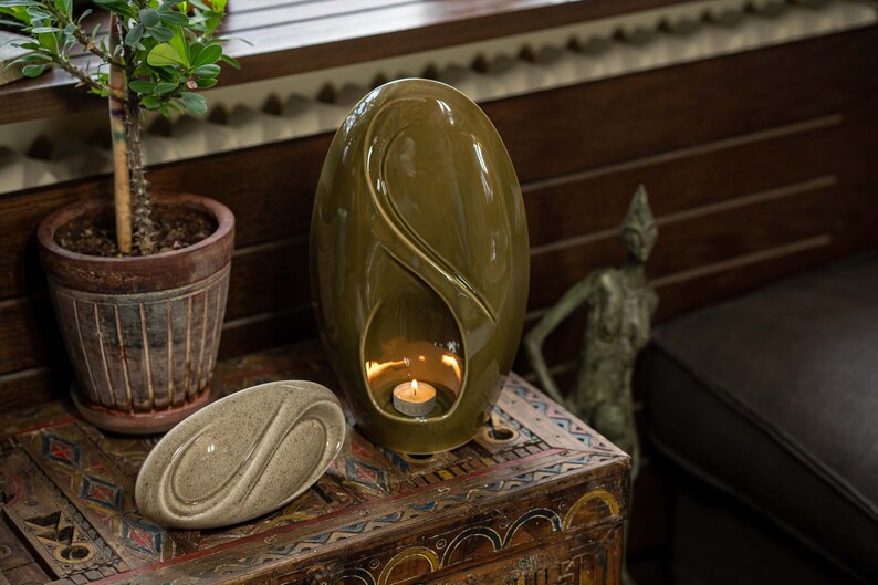 Adult size urn for ashes Eternity. The urn represents a straight ellipse with a hint of the infinity symbol all along its length. There is a place for a candle in the bottom half of the urn. This ceramic art urn comes in a various colors. By Pulvis