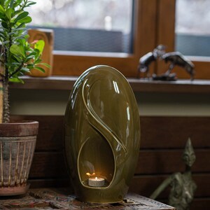 Adult size urn for ashes Eternity. The urn represents a straight ellipse with a hint of the infinity symbol all along its length. There is a place for a candle in the bottom half of the urn. This ceramic art urn comes in a various colors. By Pulvis