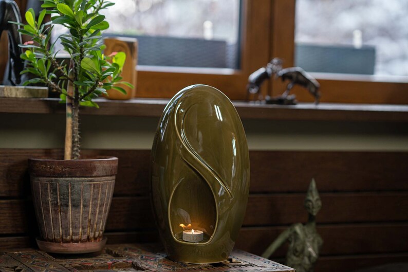 Adult size urn for ashes Eternity. The urn represents a straight ellipse with a hint of the infinity symbol all along its length. There is a place for a candle in the bottom half of the urn. This ceramic art urn comes in a various colors. By Pulvis