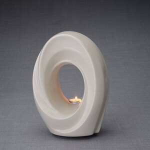 The Passage is a unique art urn for ashes. It represents a spiral, a vortex with a hole in the middle. The ashes go inside the walls and there is a candle that when lit reflects on the inner side of the art urn. This urn comes in a transparent color.