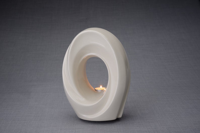 The Passage is a unique art urn for ashes. It represents a spiral, a vortex with a hole in the middle. The ashes go inside the walls and there is a candle that when lit reflects on the inner side of the art urn. This urn comes in a transparent color.