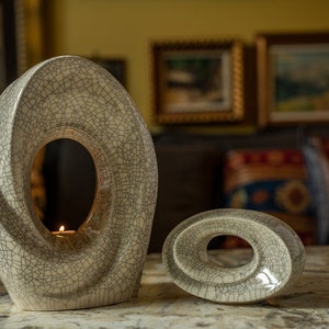 The Passage is a unique art urn for ashes. It represents a spiral with a hole in the middle. The ashes go inside the walls and there is a candle that when lit reflects on the inner side of the urn. This is a photo of a large urn and keepsake.