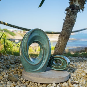 This unique keepsake urn represents a horizontal ellipse with a hole in the middle. Shaped as a spiral, a vortex, this handmade memorial urn holds the ashes in its walls. Set of urns The Passage large urn and keepsake.
