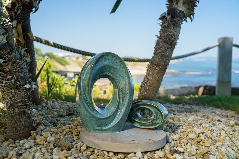 This unique keepsake urn represents a horizontal ellipse with a hole in the middle. Shaped as a spiral, a vortex, this handmade memorial urn holds the ashes in its walls. Set of urns The Passage large urn and keepsake.