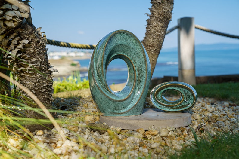 This unique keepsake urn represents a horizontal ellipse with a hole in the middle. Shaped as a spiral, a vortex, this handmade memorial urn holds the ashes in its walls. Set of urns The Passage large urn and keepsake.