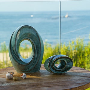 This unique keepsake urn represents a horizontal ellipse with a hole in the middle. Shaped as a spiral, a vortex, this handmade memorial urn holds the ashes in its walls. Set of urns The Passage large urn and keepsake.