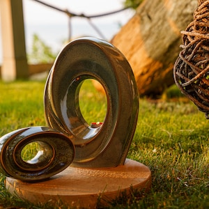 This unique keepsake urn represents a horizontal ellipse with a hole in the middle. Shaped as a spiral, a vortex, this handmade memorial urn holds the ashes in its walls. Set of urns The Passage large urn and keepsake.