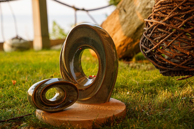 This unique keepsake urn represents a horizontal ellipse with a hole in the middle. Shaped as a spiral, a vortex, this handmade memorial urn holds the ashes in its walls. Set of urns The Passage large urn and keepsake.