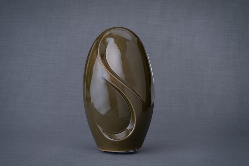 Adult size urn for ashes Eternity. The urn represents a straight ellipse with a hint of the infinity symbol all along its length. There is a place for a candle in the bottom half of the urn. This ceramic art urn comes in a various colors. By Pulvis