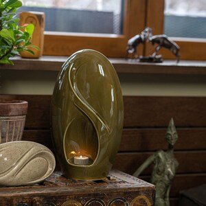 Adult size urn for ashes Eternity. The urn represents a straight ellipse with a hint of the infinity symbol all along its length. There is a place for a candle in the bottom half of the urn. This ceramic art urn comes in a various colors. By Pulvis