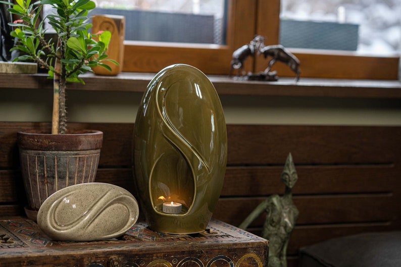 Adult size urn for ashes Eternity. The urn represents a straight ellipse with a hint of the infinity symbol all along its length. There is a place for a candle in the bottom half of the urn. This ceramic art urn comes in a various colors. By Pulvis
